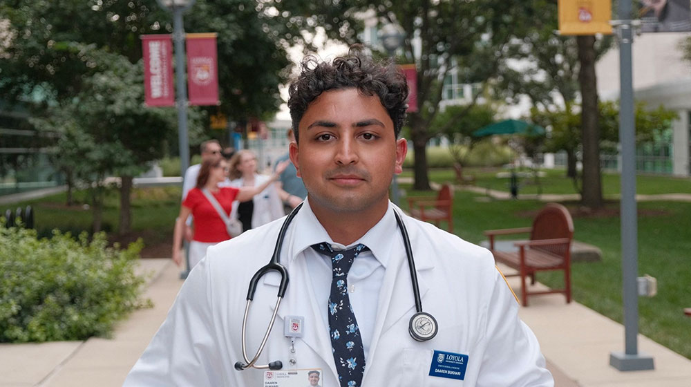 Daaren Bukhari wearing his white lab coat with a stethoscope around his neck while standing outside 
